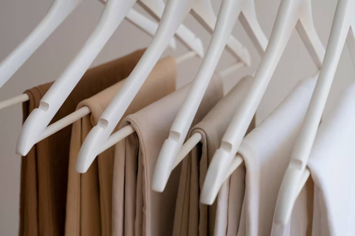 A collection of neutral-toned clothing neatly hung on white hangers, showcasing varying shades of beige and cream.