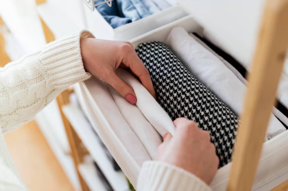 A person wearing a cream sweater organizes folded clothes in a white drawer, showcasing neatly arranged items in various patterns.