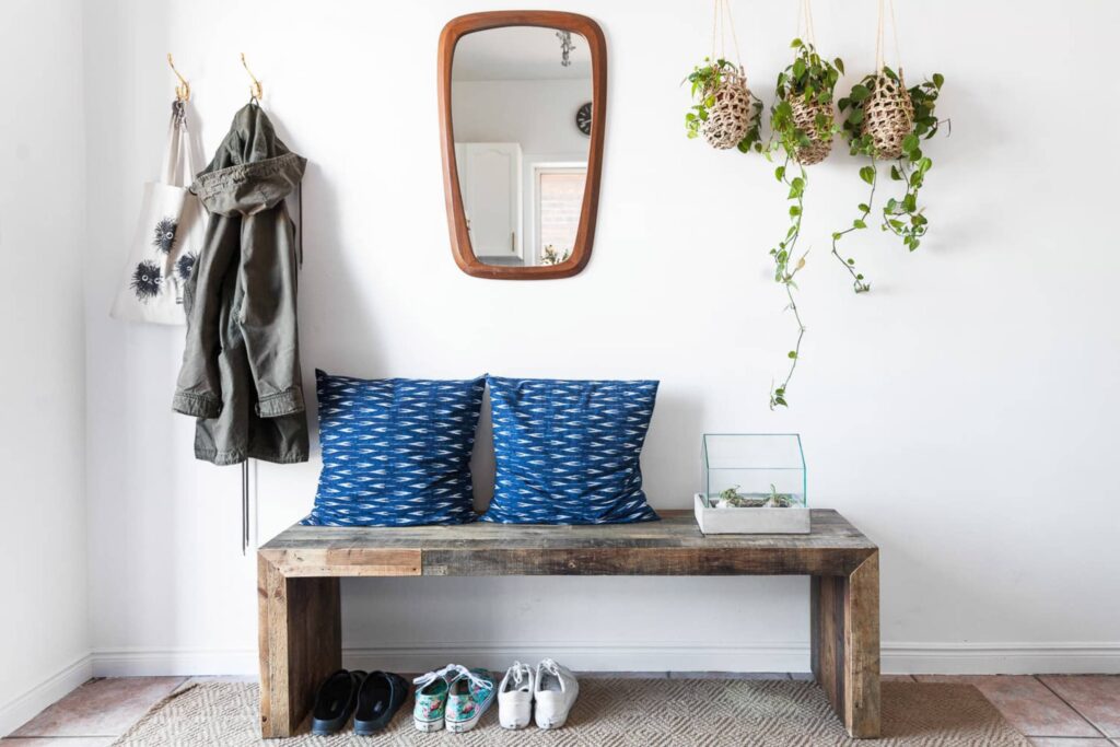 A modern entryway featuring a wooden console table, mirror, coat rack, and black front door, adorned with a plant and stylish decor.