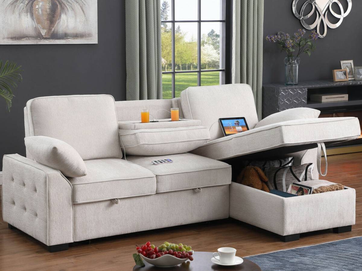 A stylish, light-colored sectional sofa with storage, two drinks, and a tablet, set in a cozy room with a large window.