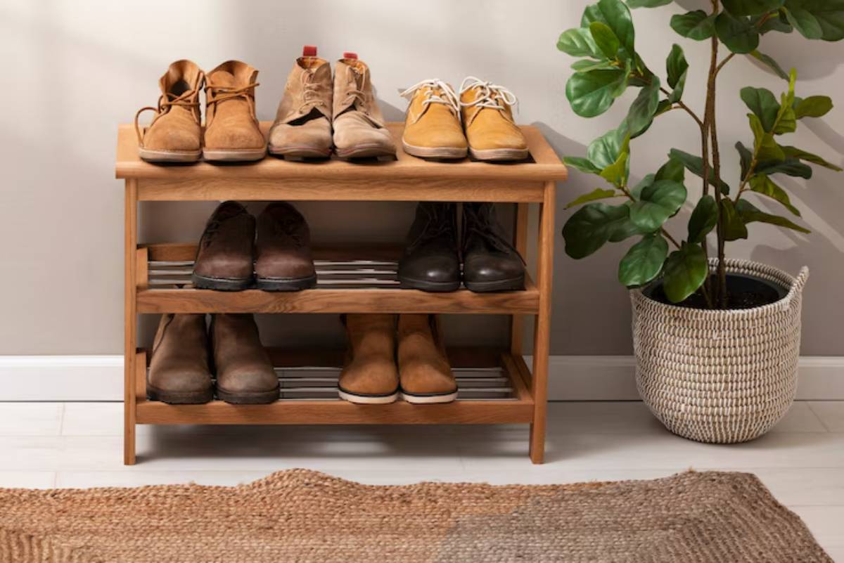 A wooden shoe rack displays various styles of boots, paired with a decorative potted plant and a textured woven mat on the floor.