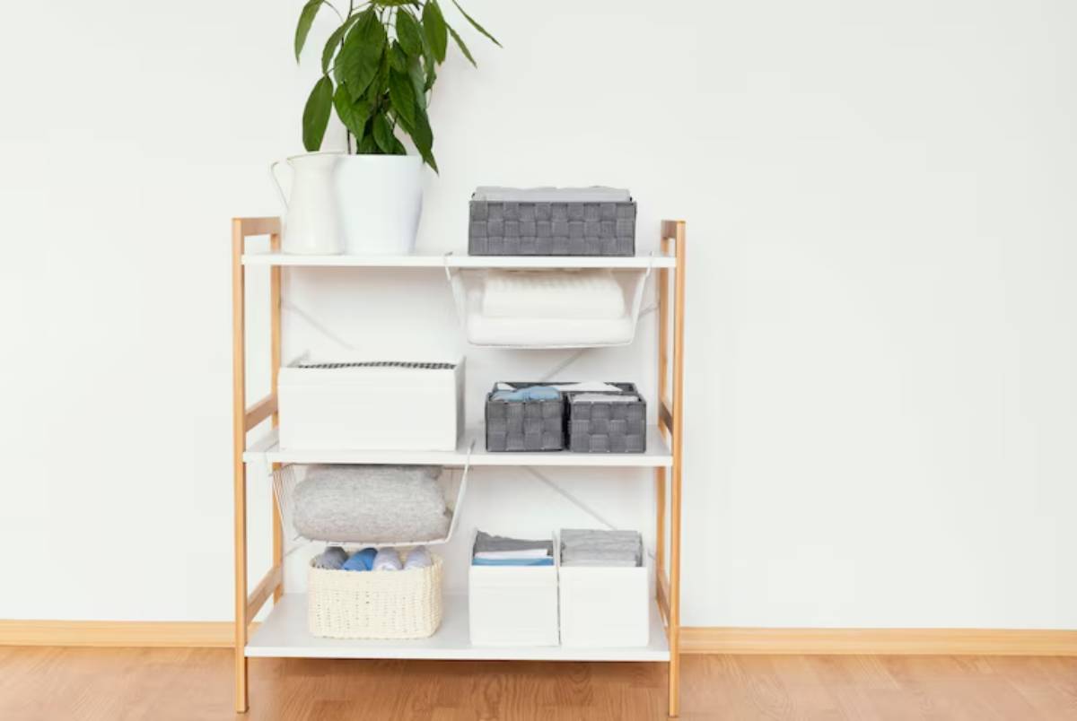A tidy shelf with white and gray storage boxes, neatly folded blankets, and a potted plant on top, against a plain wall.