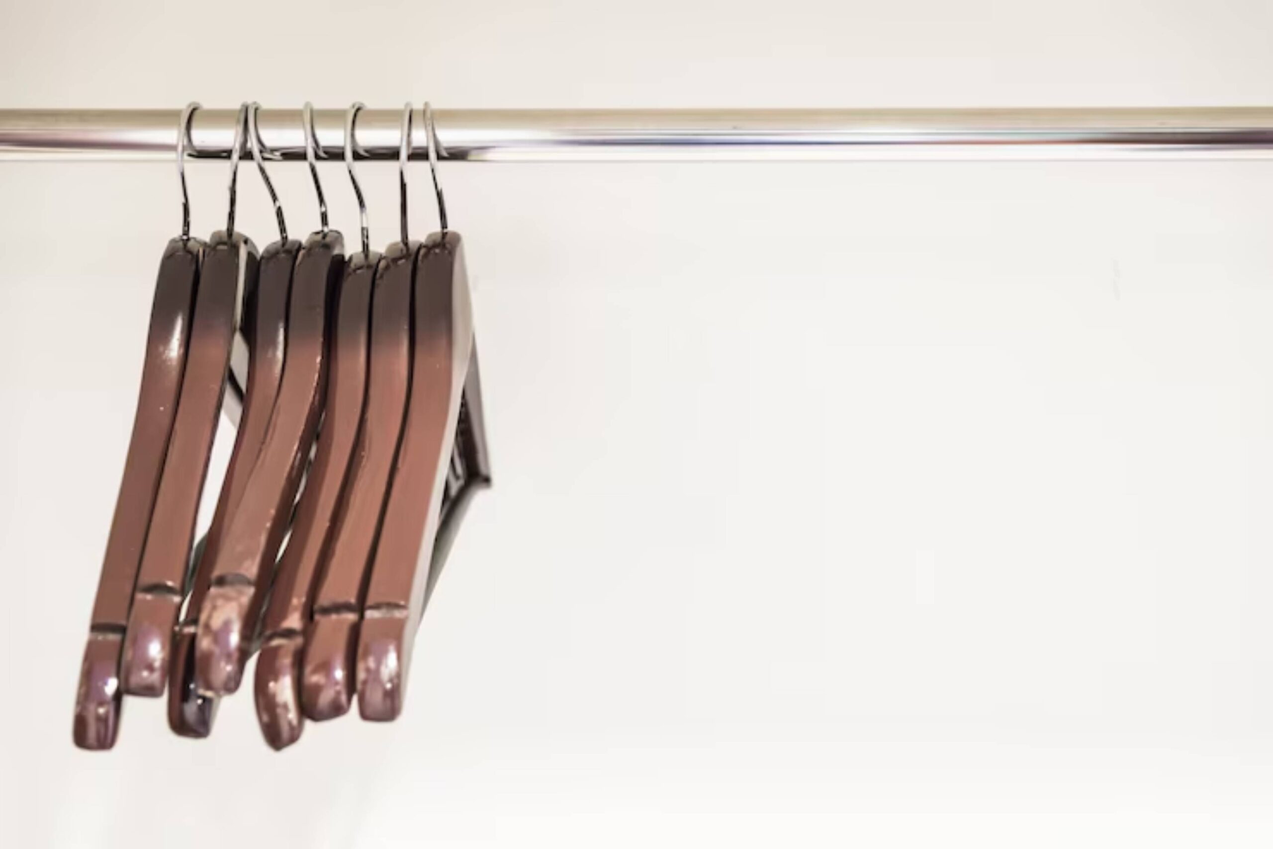Five sleek brown hangers suspended on a chrome rod against a minimalistic white background.
