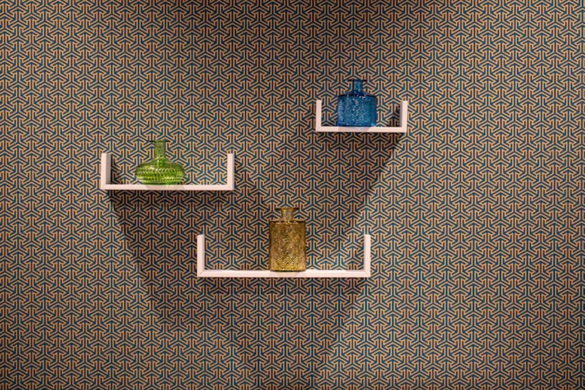 Three colorful glass vases on white shelves against a geometric patterned wallpaper.