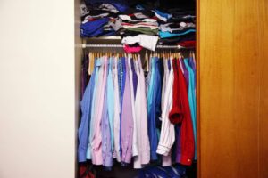 A wooden closet filled with neatly hung shirts in various colors, with neatly stacked t-shirts on top.