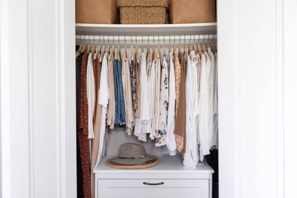 A stylish bedroom and closet featuring organized clothing, shoes, and accessories, with a cozy bed and soft textiles.