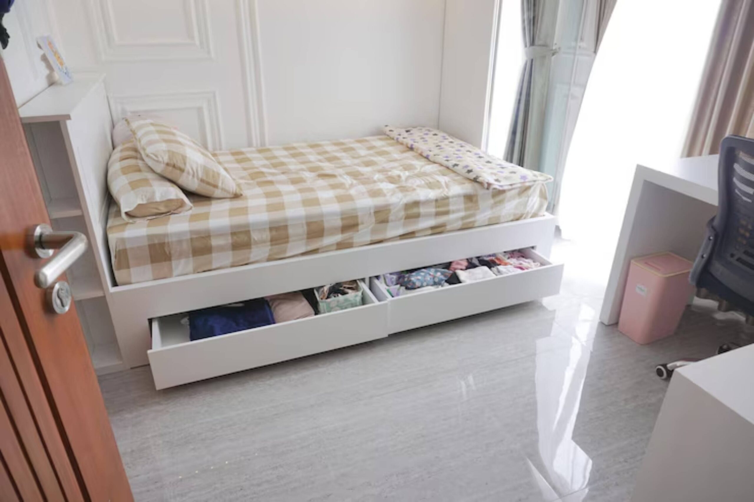 Cozy bedroom featuring a twin bed with checkered bedding, storage drawers underneath, a desk, and natural light from a window.