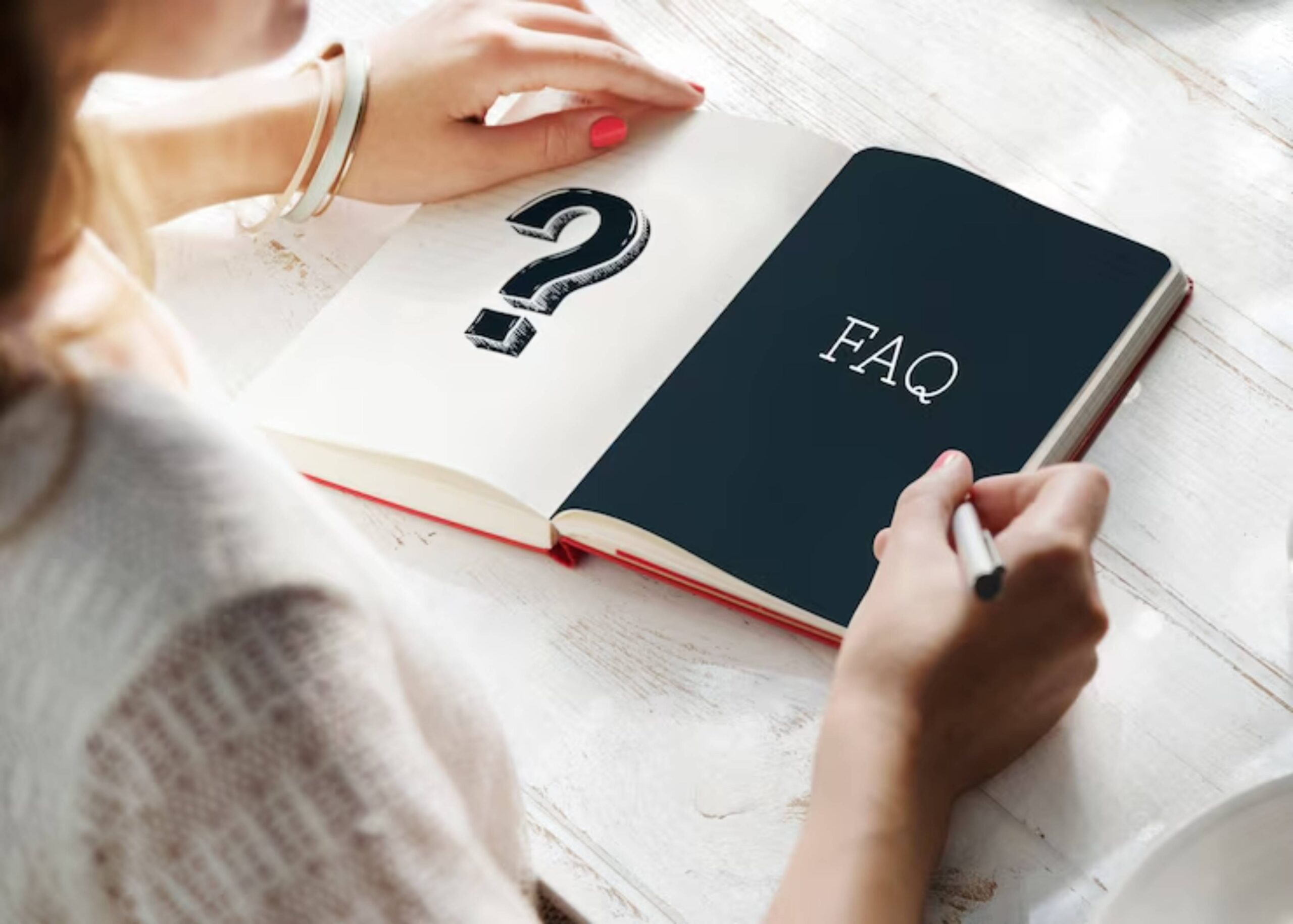 A person writes in a notebook; one page features a question mark, while the other displays FAQ in white text on a dark background.