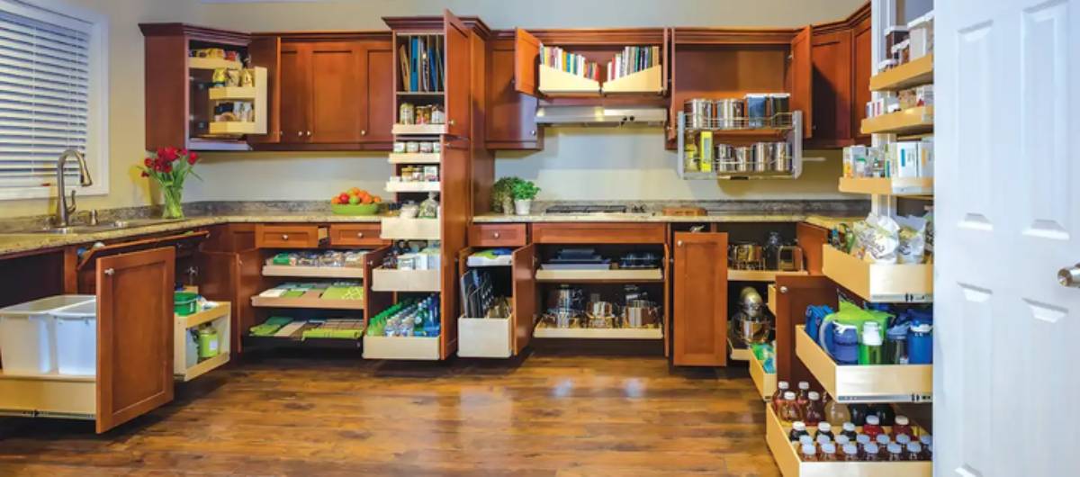 A well-organized kitchen featuring wooden cabinets, open shelves with books and jars, and neatly arranged drawers for utensils and ingredients.