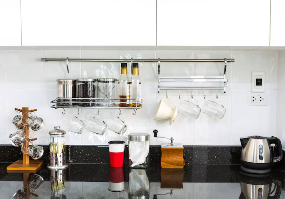 A modern kitchen setup featuring hanging mugs, spice jars, a kettle, and a sleek black countertop with various utensils and decor.